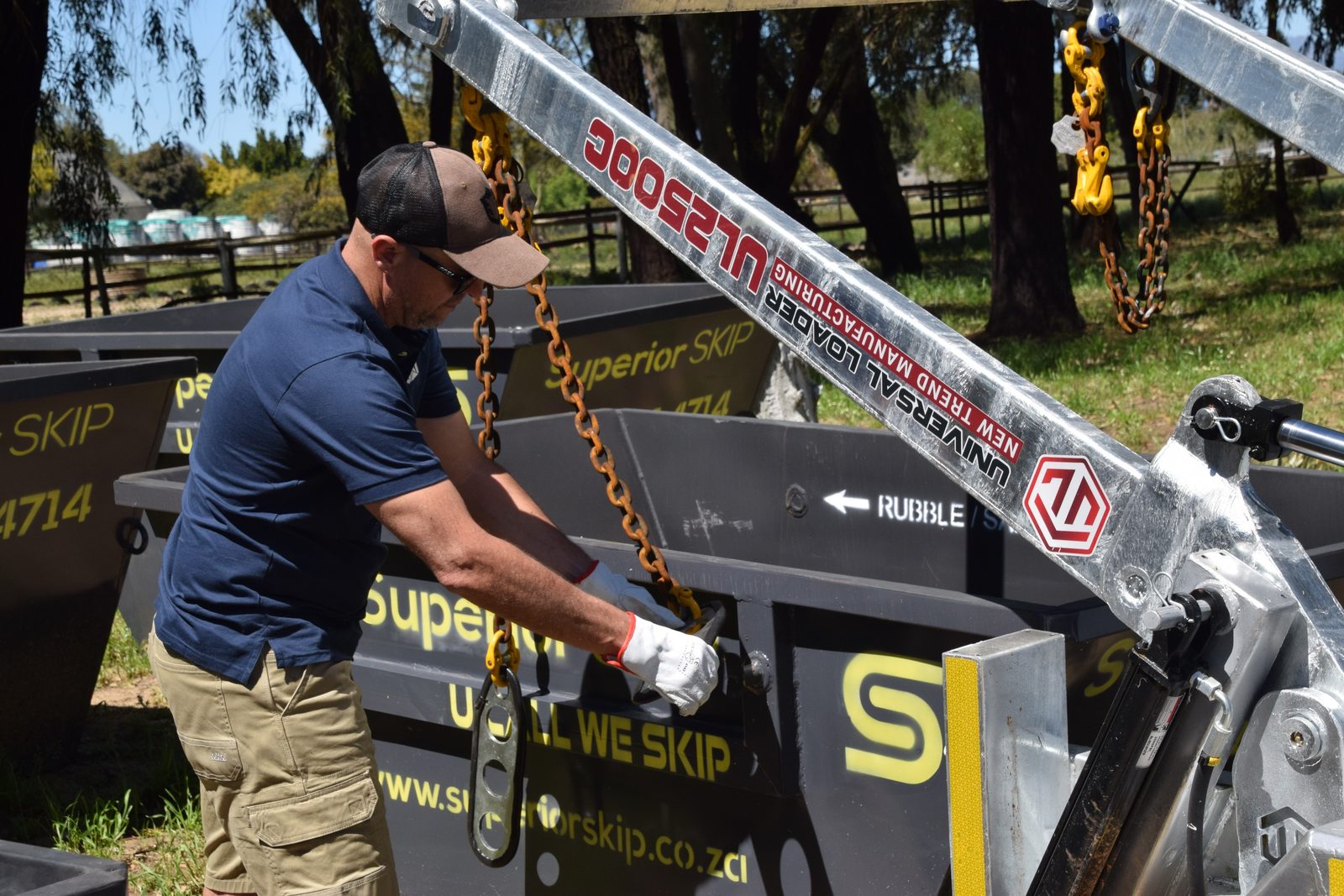 Chains being attached to lift a skip bin onto the trailer